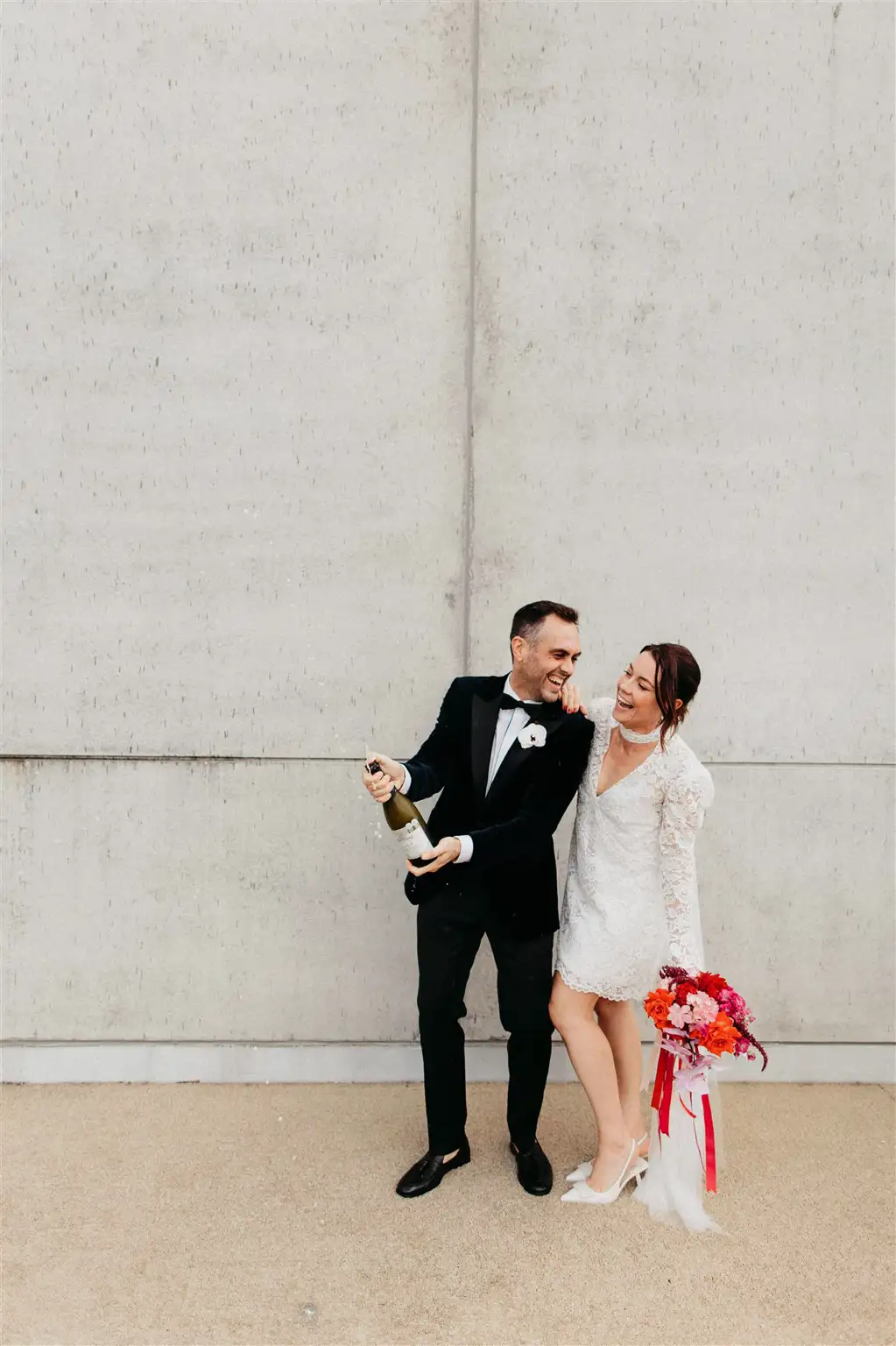 Christian and Amy sheltering under an umbrella while sharing an intimate moment against The Calile's textured exterior wall